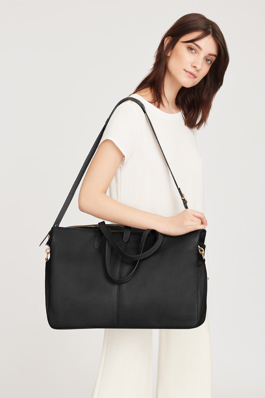 Woman standing with a large handbag over her shoulder.