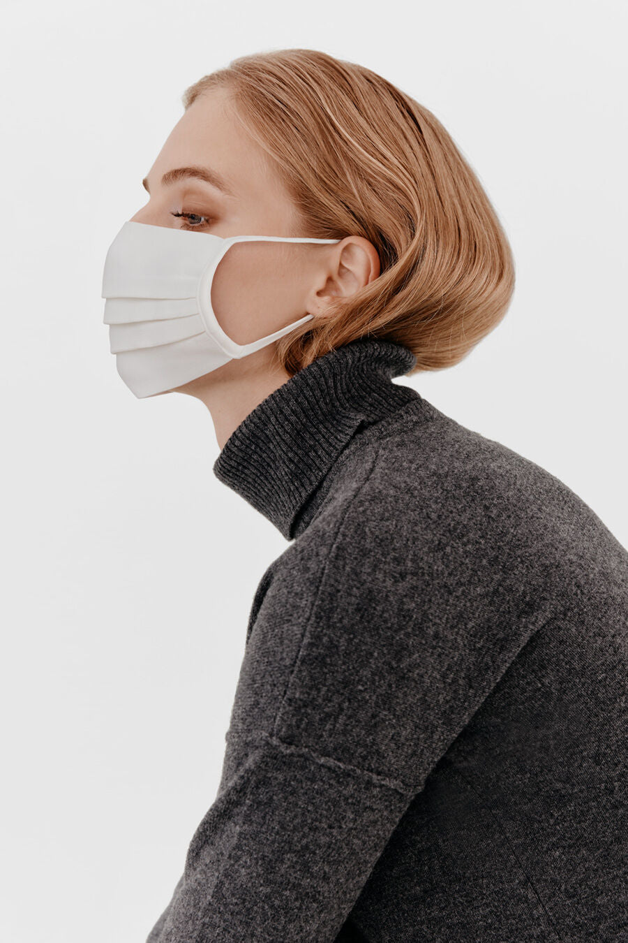 Side profile of a person wearing a mask and a turtleneck sweater.