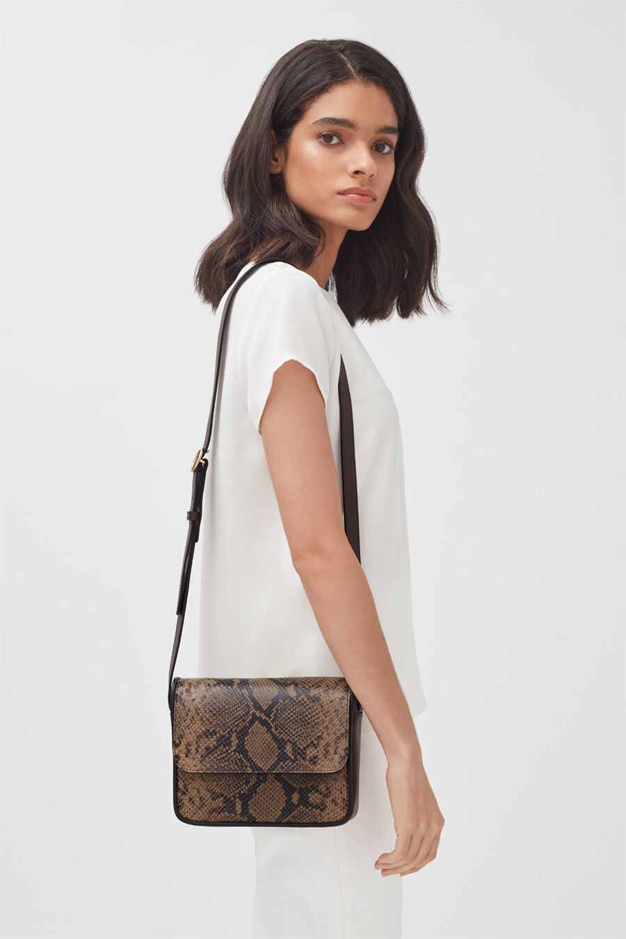 Woman standing sideways with a shoulder bag.