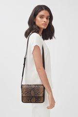 Woman standing sideways with a shoulder bag.