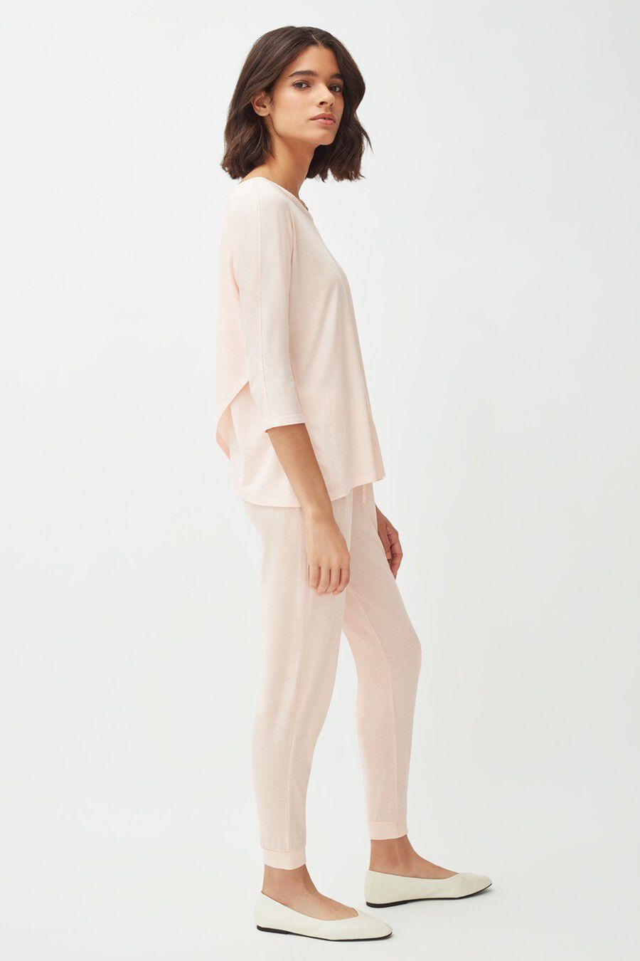Woman standing in profile wearing a casual outfit and flat shoes.