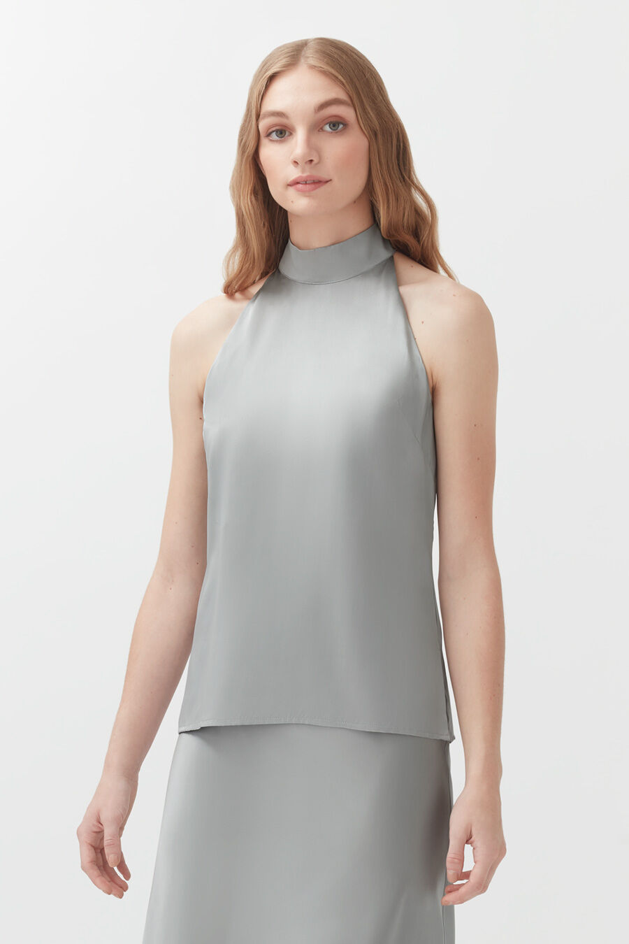 Woman in a sleeveless top and skirt standing against a plain background.