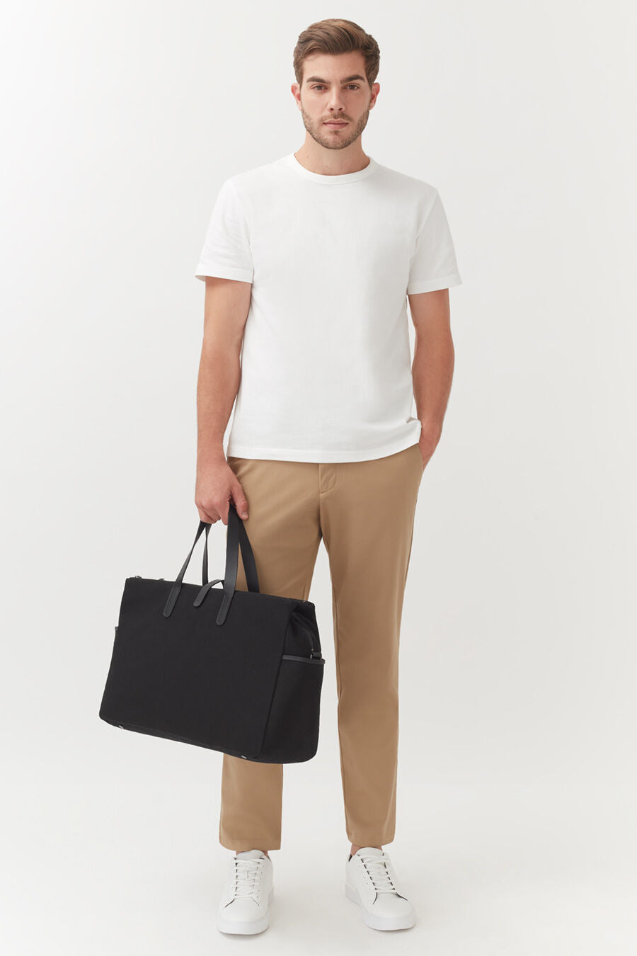 Man standing holding a bag and wearing a T-shirt and pants.