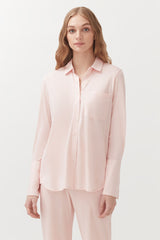 Woman in a button-up shirt and matching pants standing against a plain backdrop.