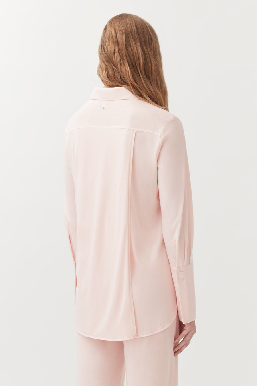 Woman viewed from the back wearing a long-sleeve shirt and trousers.