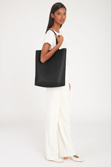 Woman standing holding a large tote bag, wearing a top and pants.