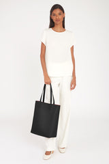 Woman standing holding a tote bag and wearing a short-sleeved top and trousers.