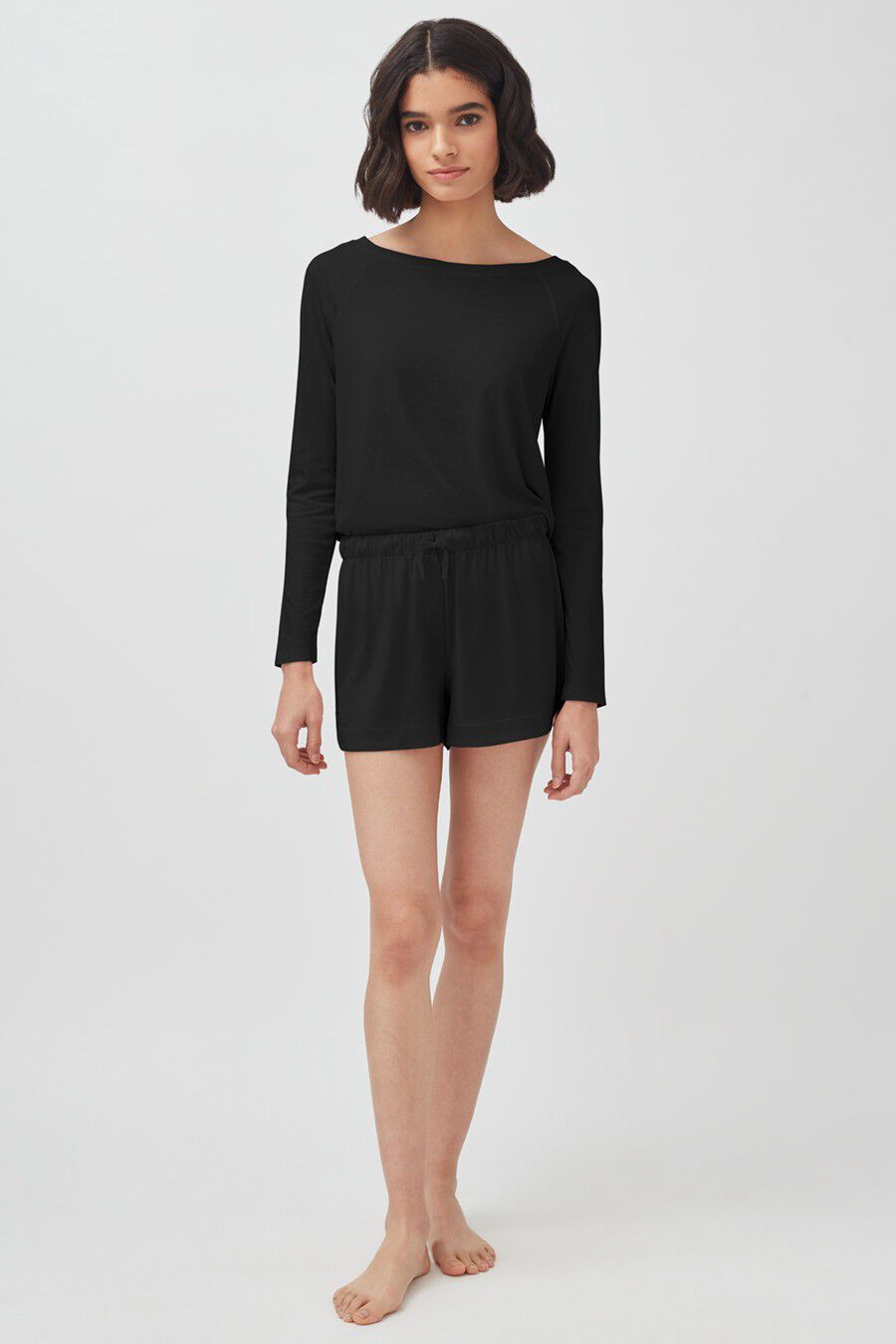 Woman standing in a long sleeve top and shorts, looking at the camera.