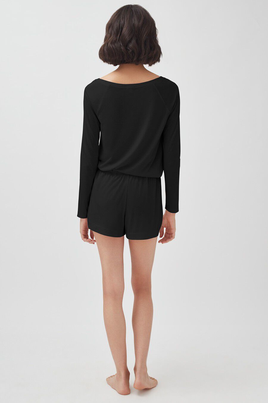 Woman standing back to the camera wearing a long-sleeve top and shorts.