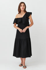 Woman in dress with one shoulder strap and ruffled layers, standing straight.
