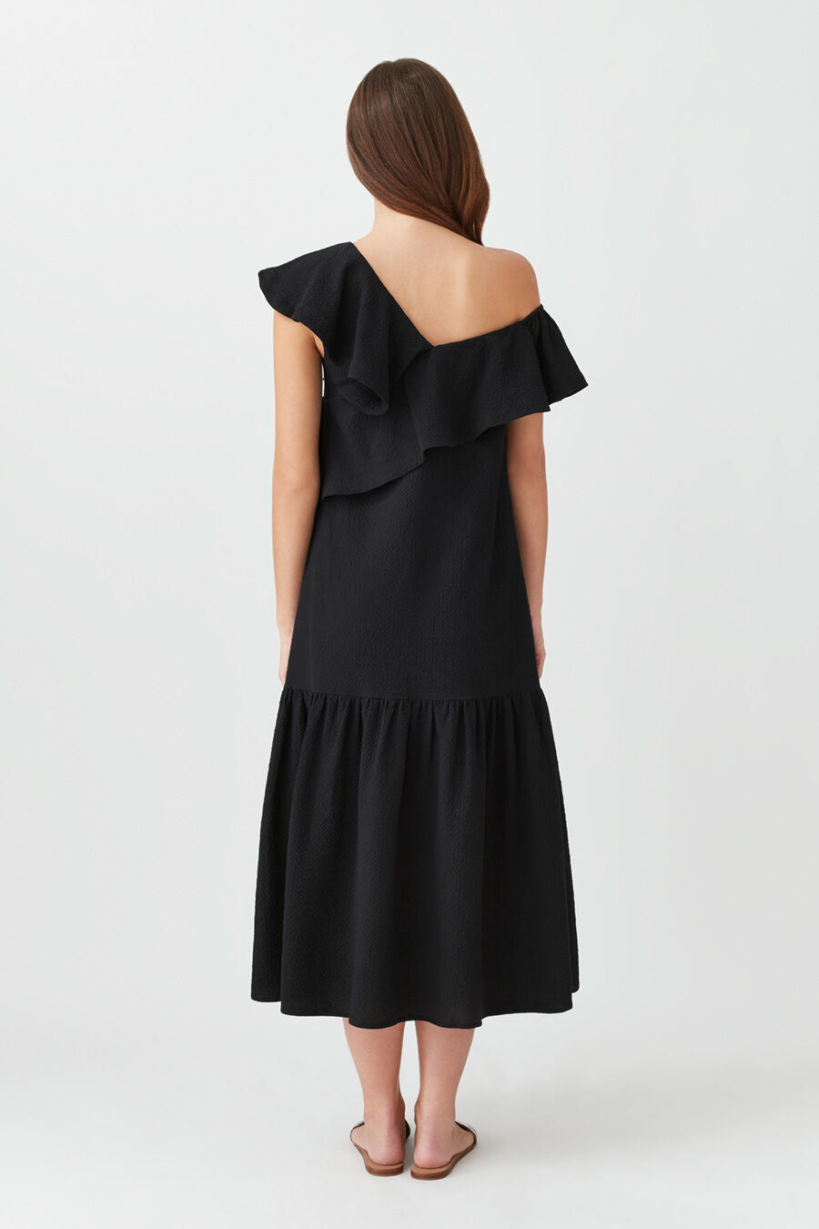Woman standing facing away, wearing a ruffled off-shoulder dress.