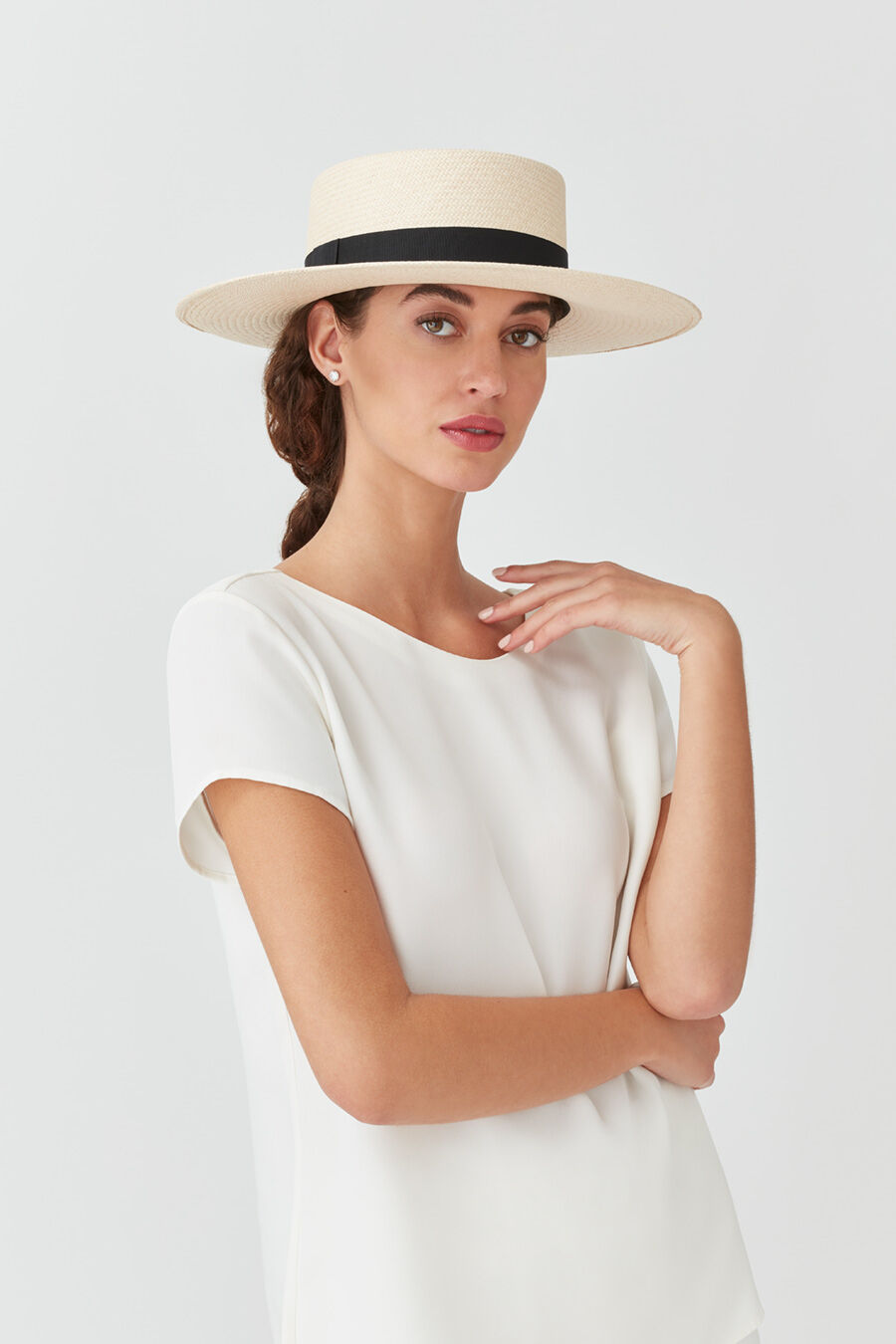 Woman wearing a wide-brimmed hat and a blouse, posing with hand on neck.