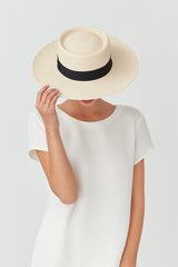 Person holding brim of hat over face, wearing a simple top.