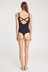 Woman standing facing away, wearing a leotard with a crisscross back design