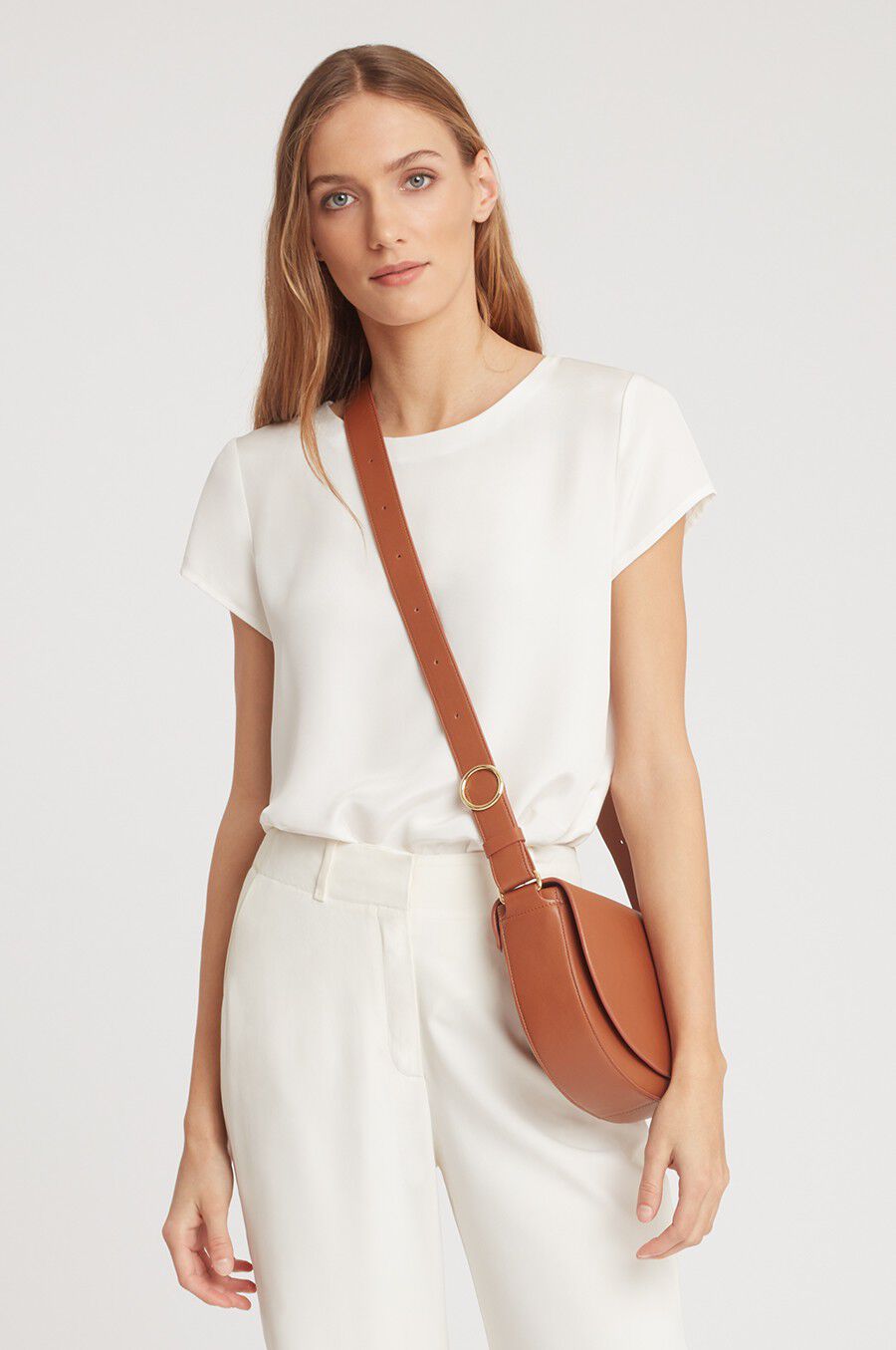 Woman standing with a crossbody bag and a casual outfit.