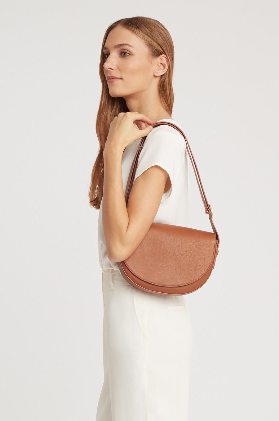 Woman standing with her hand on her shoulder carrying a purse.