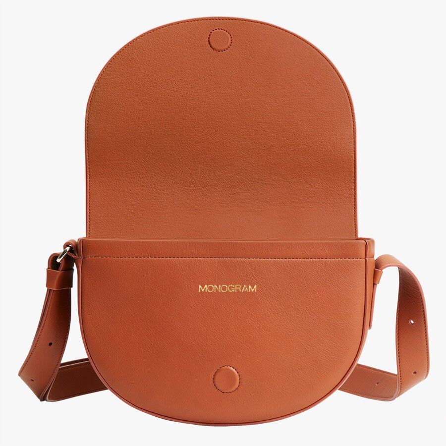 Round leather shoulder bag with flap and adjustable strap.