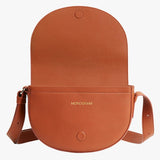 Round leather shoulder bag with flap and adjustable strap.