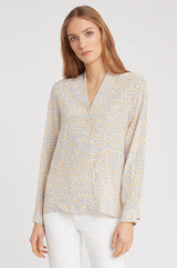 Woman wearing a long-sleeved blouse and white pants standing upright.